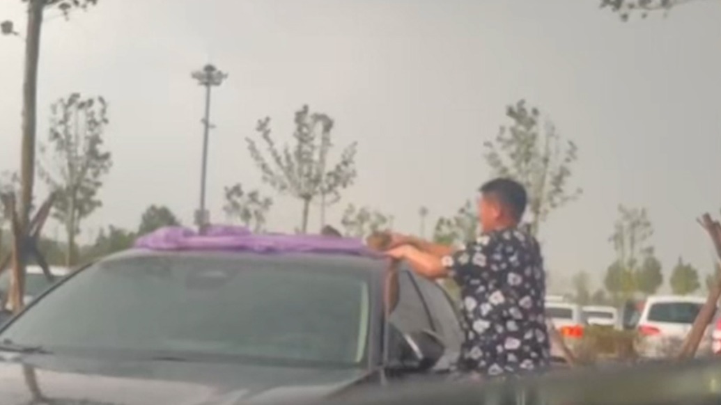 山東游客雨天忘關(guān)轎車天窗，河南大哥拿雨衣幫忙擋雨