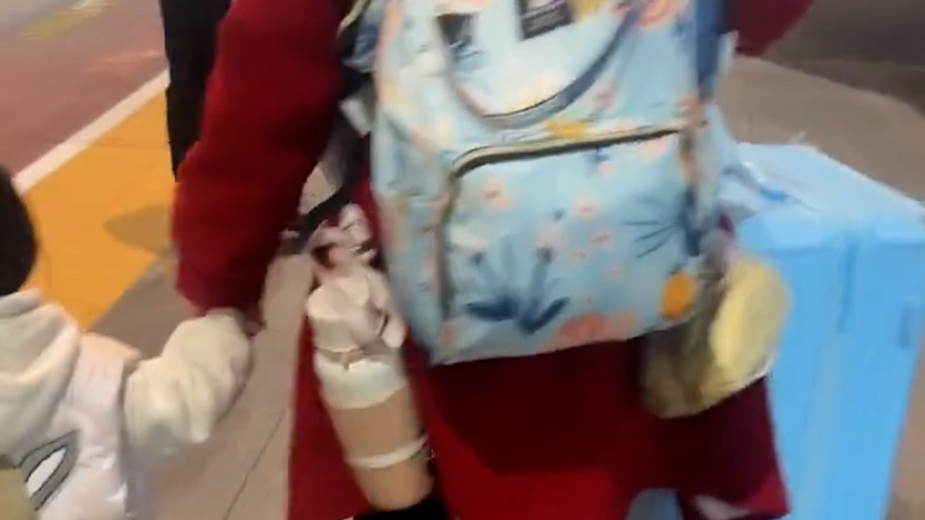女子手牽?jī)蓺q娃懷掛三月嬰推著行李箱探望丈夫，過路旅客主動(dòng)上前幫忙