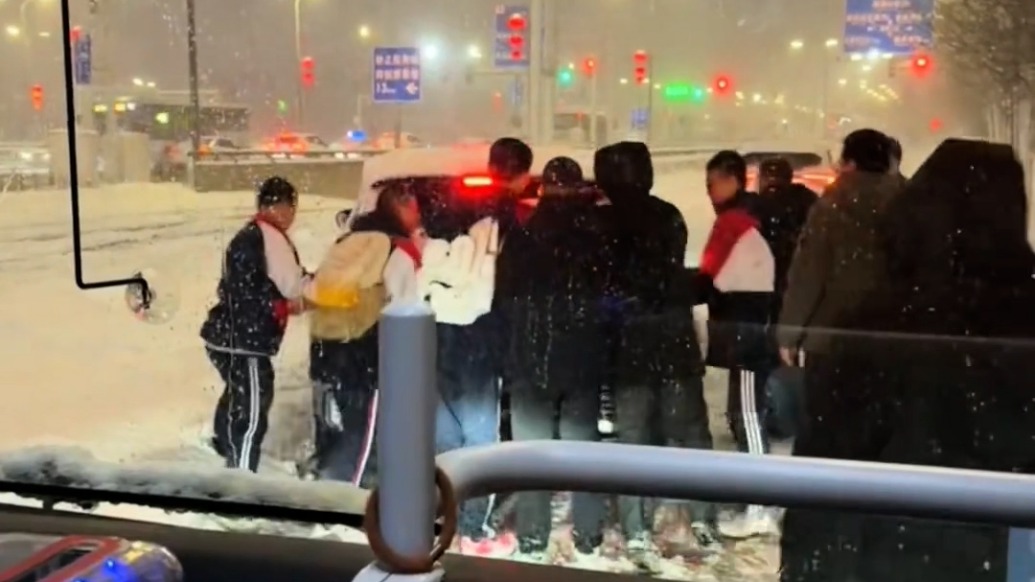 热心乘客一声号召，公交车上的男士冲下去帮推打滑轿车，车上的学生们也主动帮忙