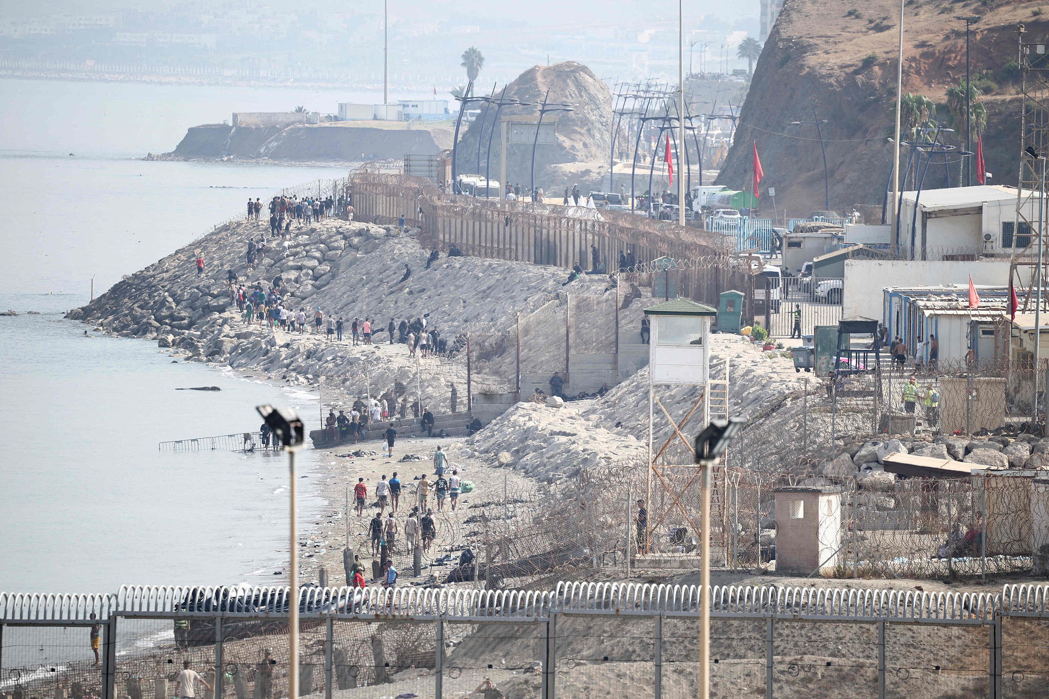 当地时间2026年8月1日，西班牙休达，人们沿摩洛哥与西班牙的北非飞地休达之间的边境围栏附近海岸线行走，返回摩洛哥。视觉中国 图